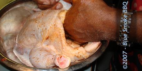 Foto van het aanbrengen van dry rub aan de binnenkant van het borstvlees van een kip ter voorbereiding van de barbeque.