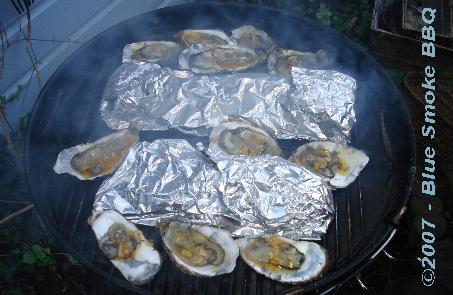 Foto van in folie ingepakte forellen en gemarineerde oesters op de barbecue door P.H.